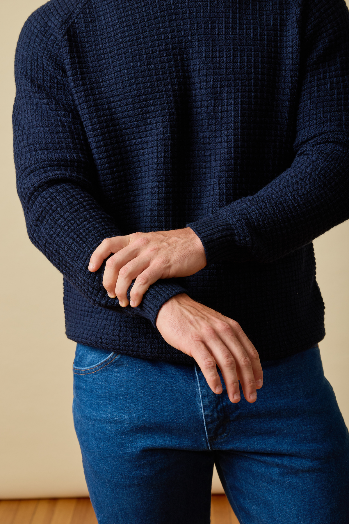 Person wearing a dark blue Sir W. Merino textured sweater and jeans against a beige background #color_navy