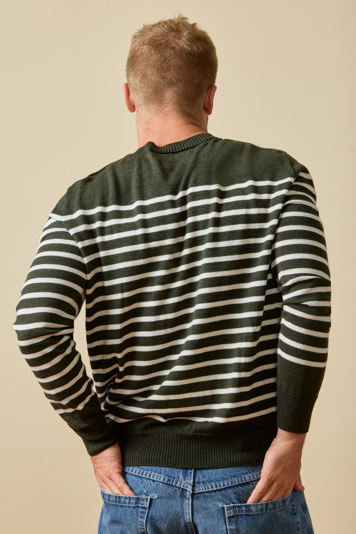 Man sitting on a wooden crate wearing a striped Merino wool sweater and jeans.