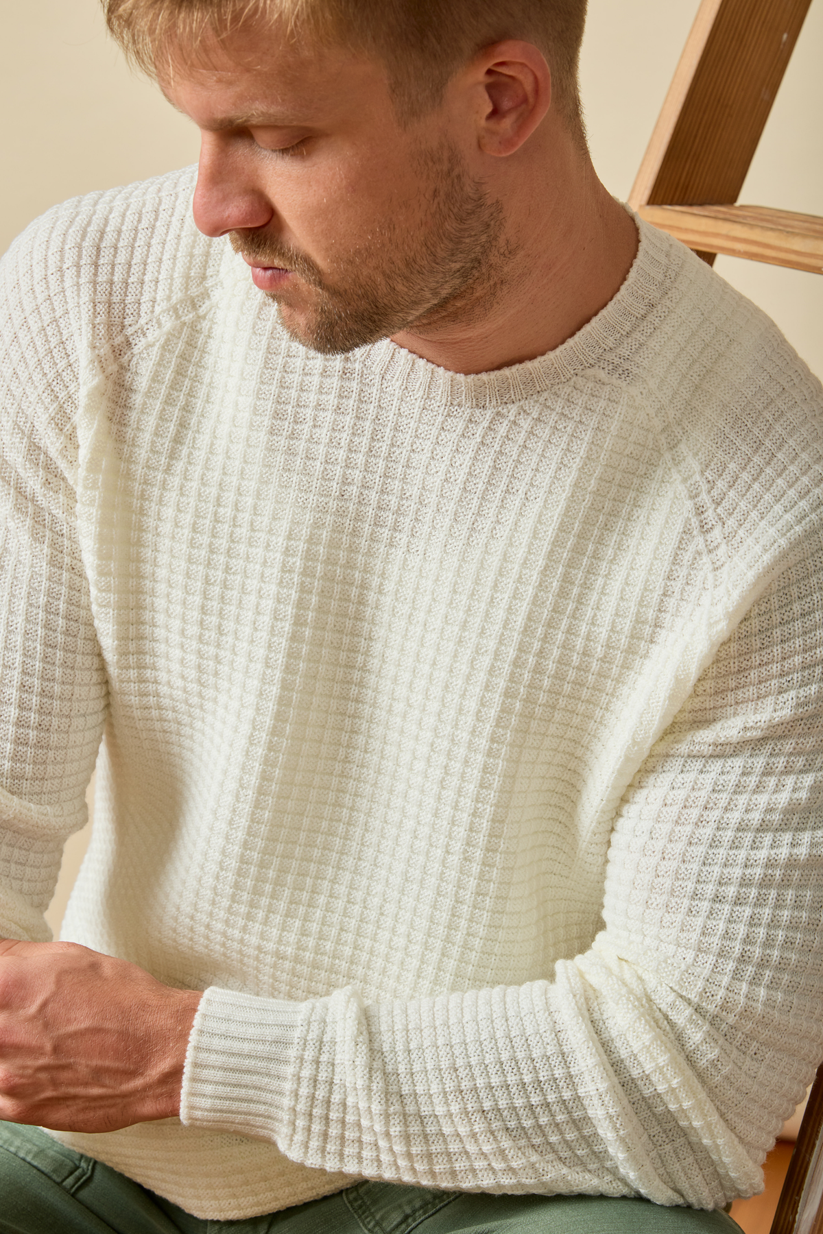 Man wearing a waffle textured cream Merino wool sweater sitting on a chair #color_naturale