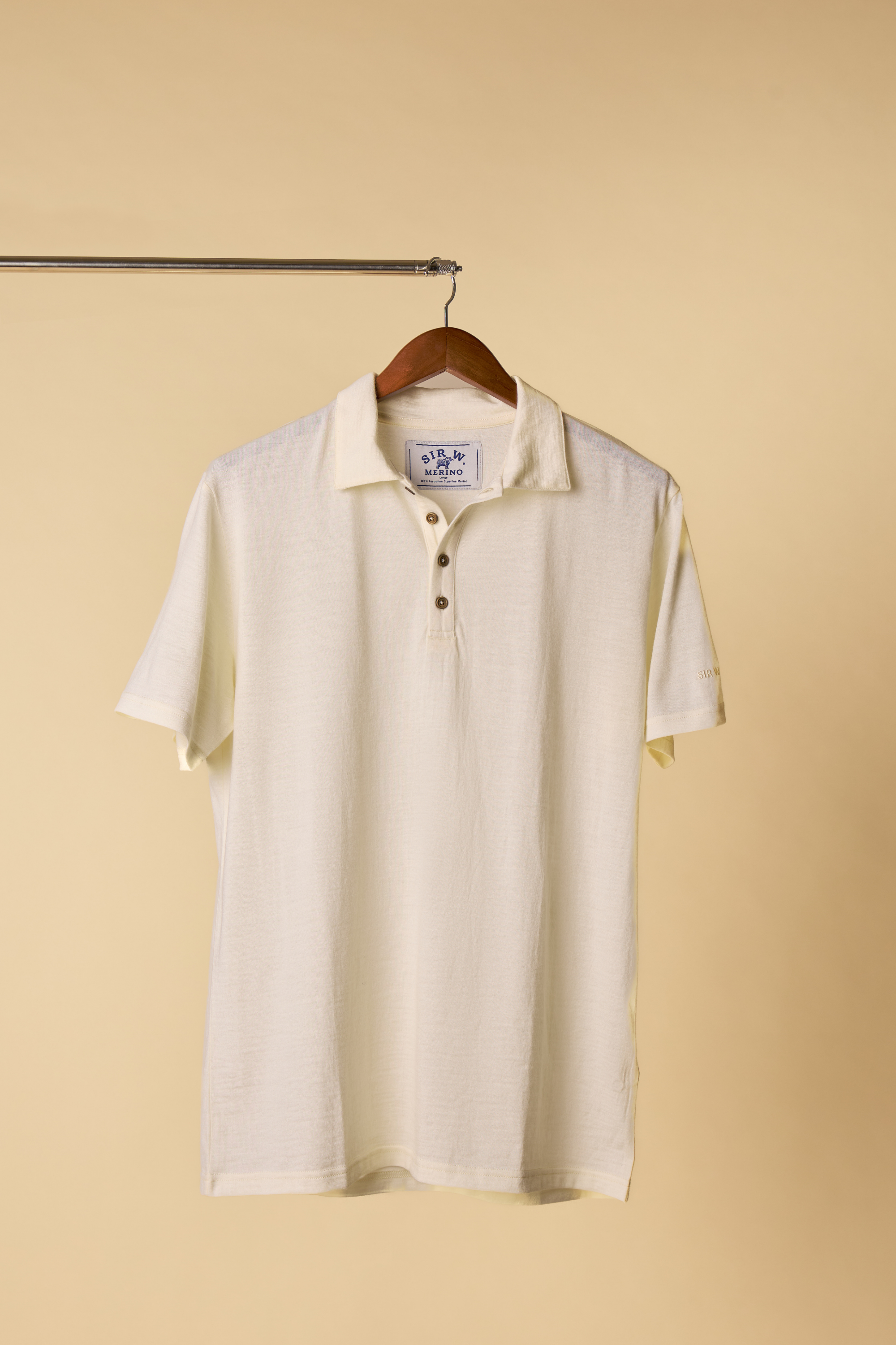 Sir W Merino white polo shirt on a hanger against a beige background