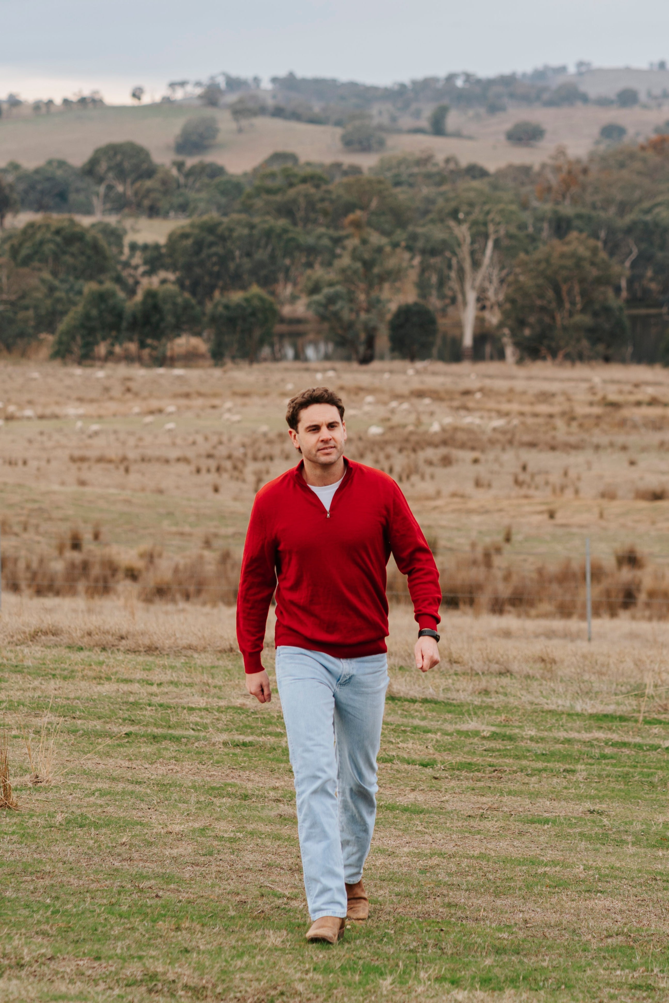 Man walking in a field with trees and hills in the background