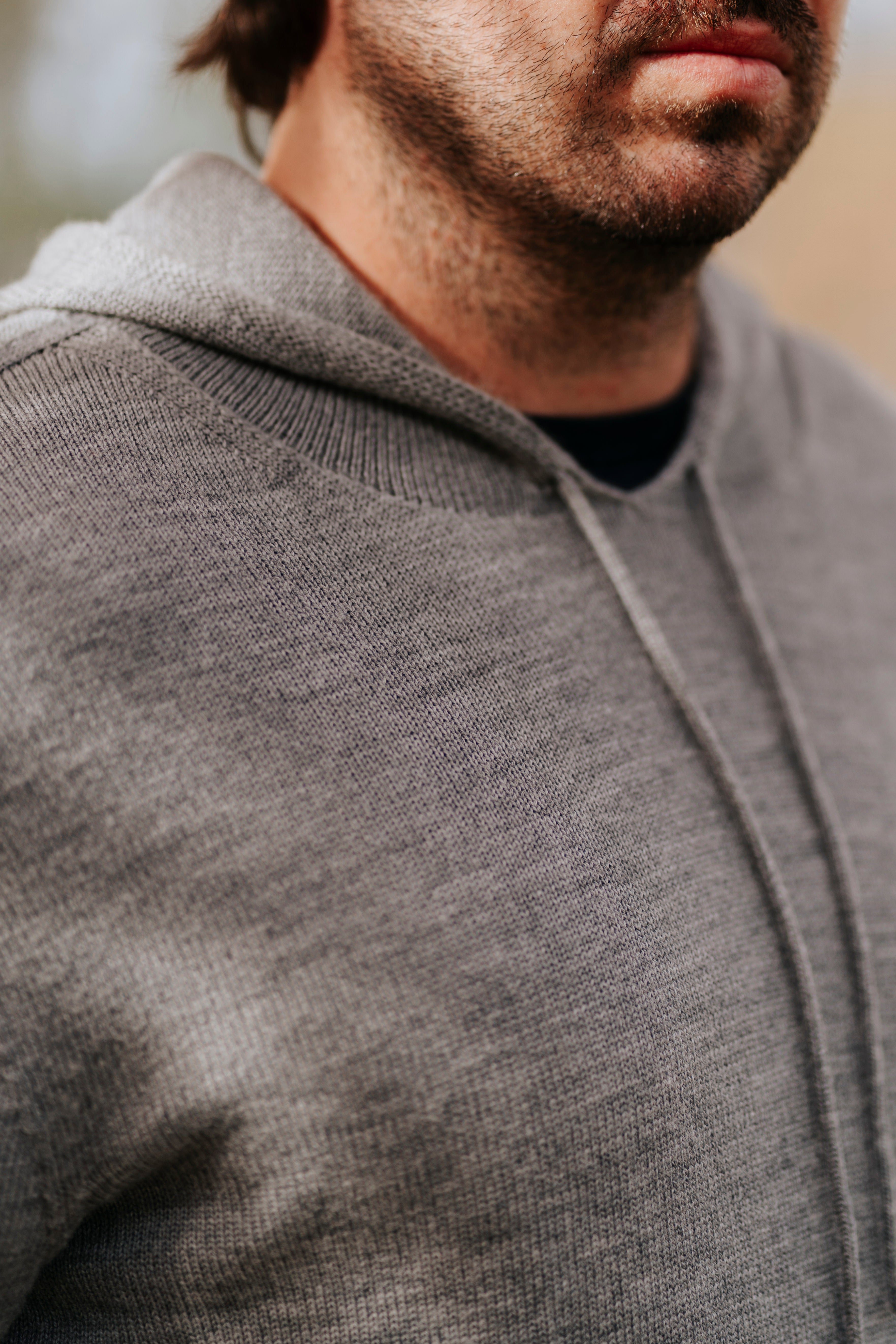 Close-up of a person wearing a gray Merino wool hoodie with a blurred background