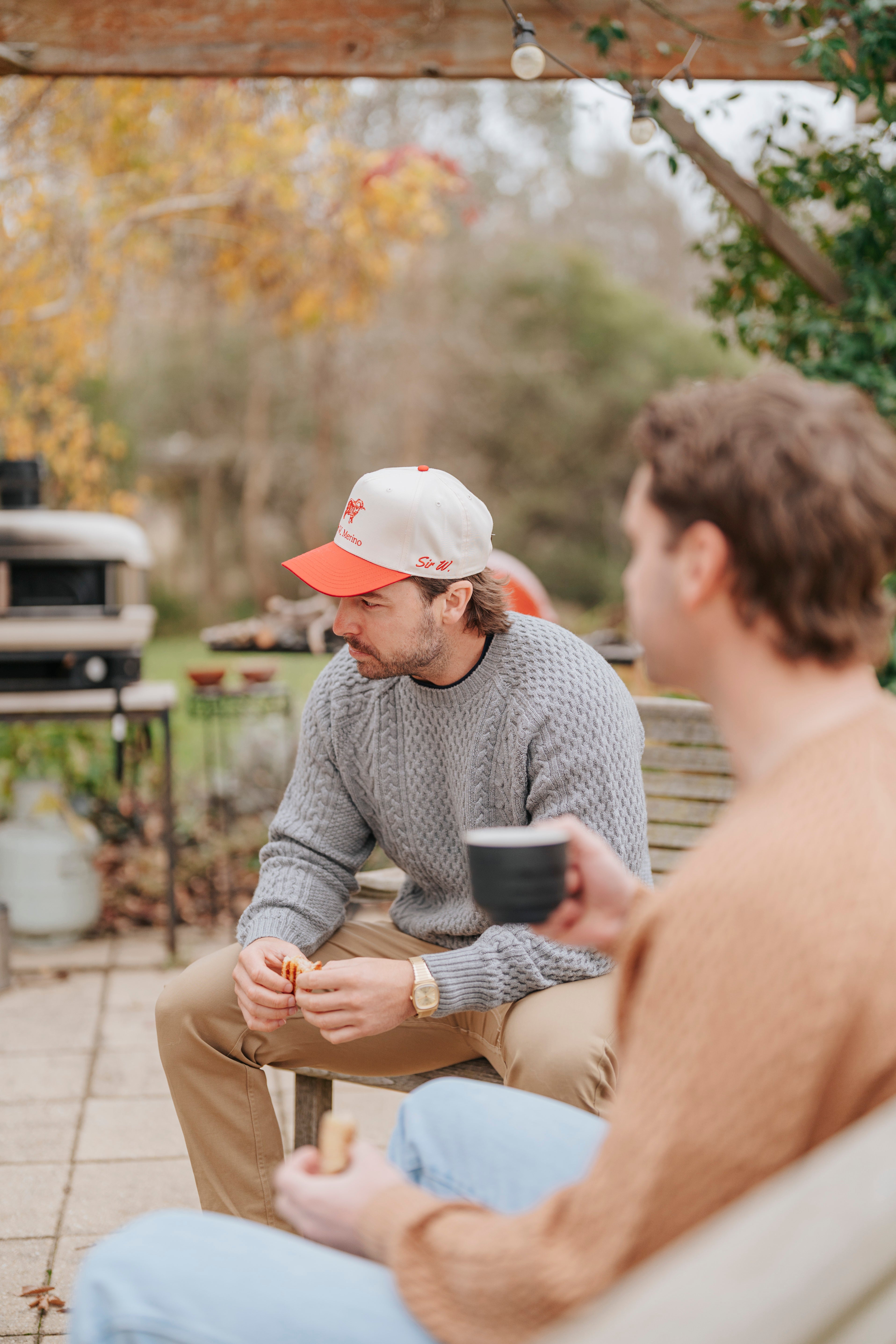 Two people sitting outdoors, one holding a coffee cup, with a garden and grill in the background.