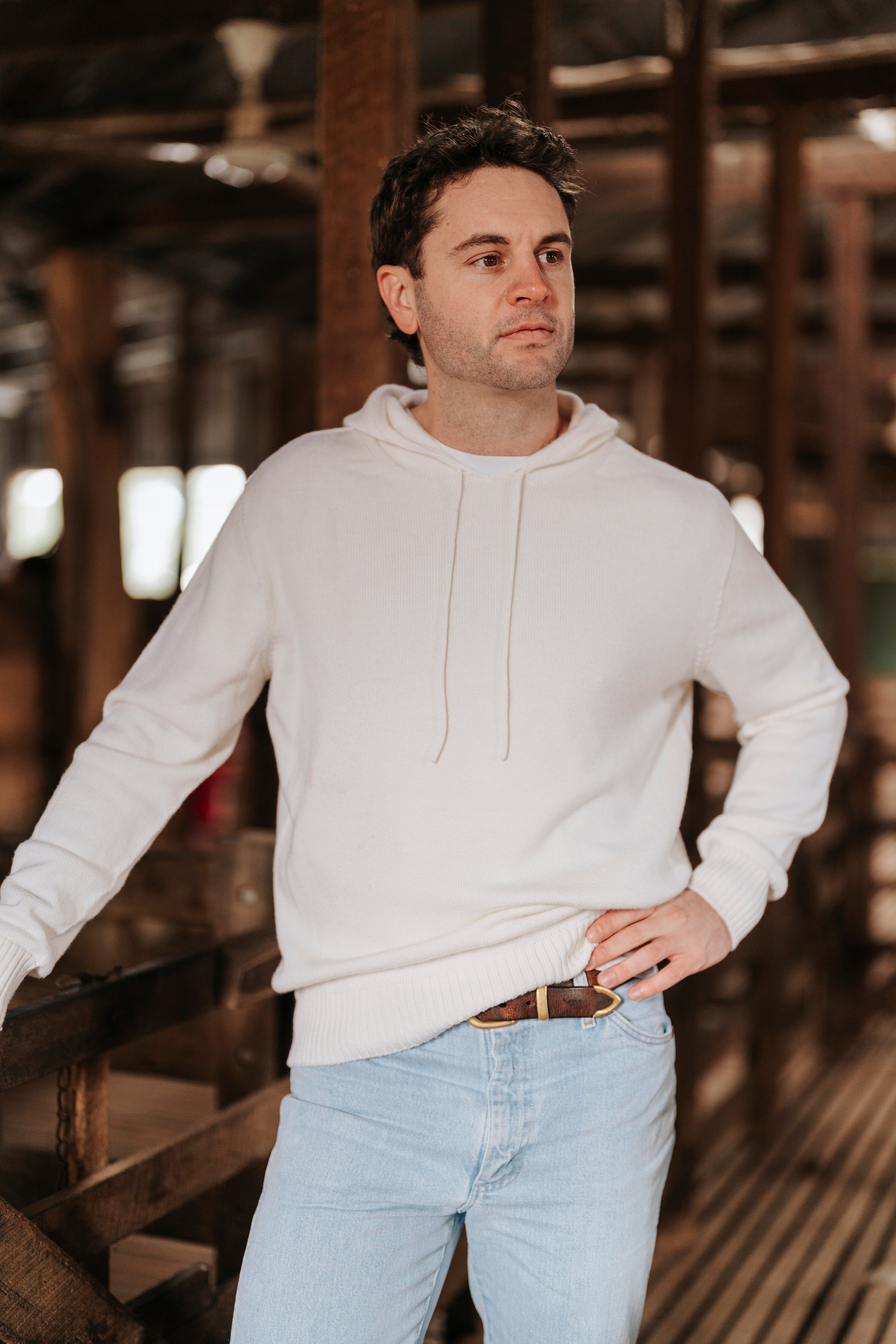 Man wearing a white hoodie and light blue jeans standing in a wooden interior.