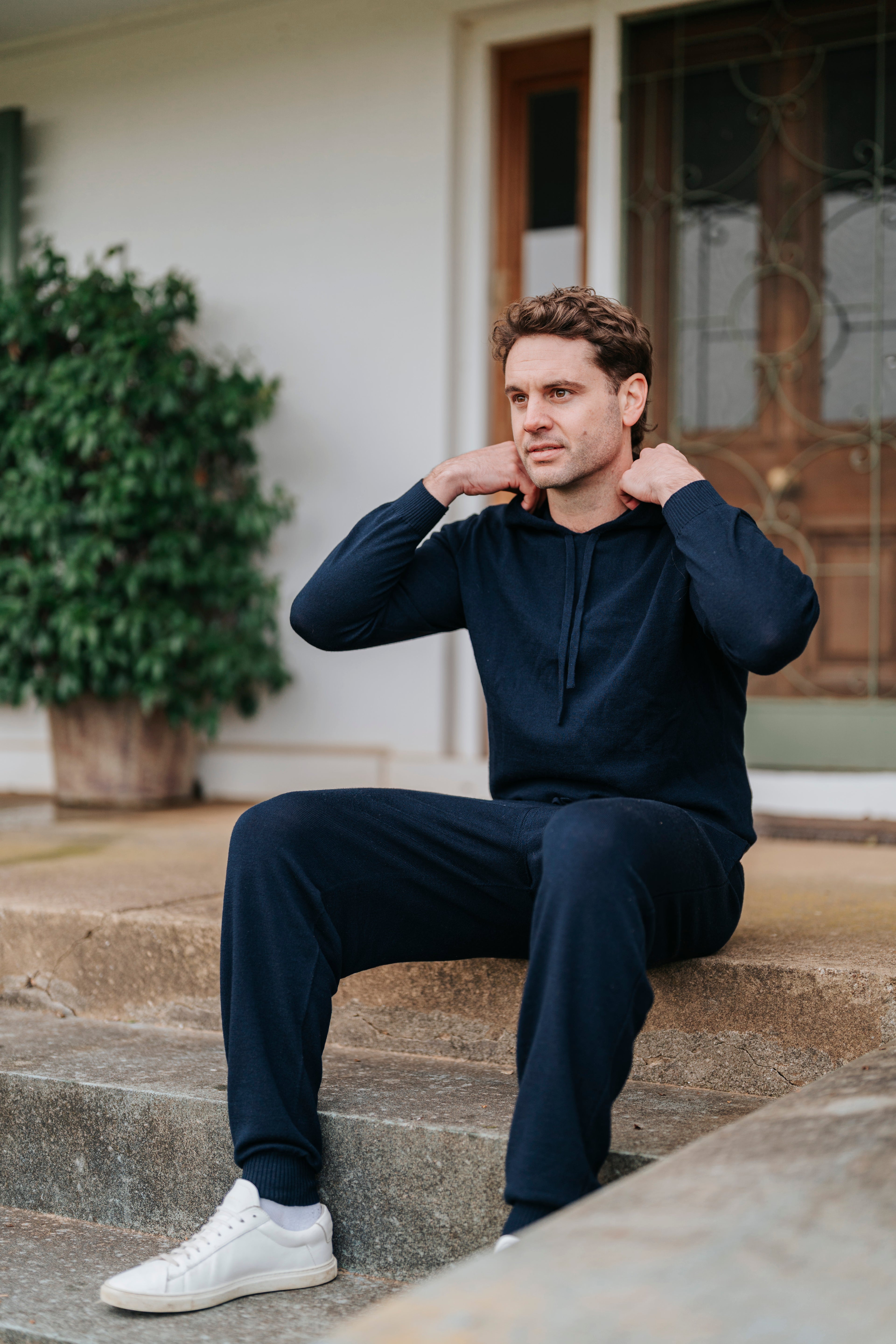Man sitting on steps wearing a Navy Merino Sweatpants tracksuit with white sneakers.
