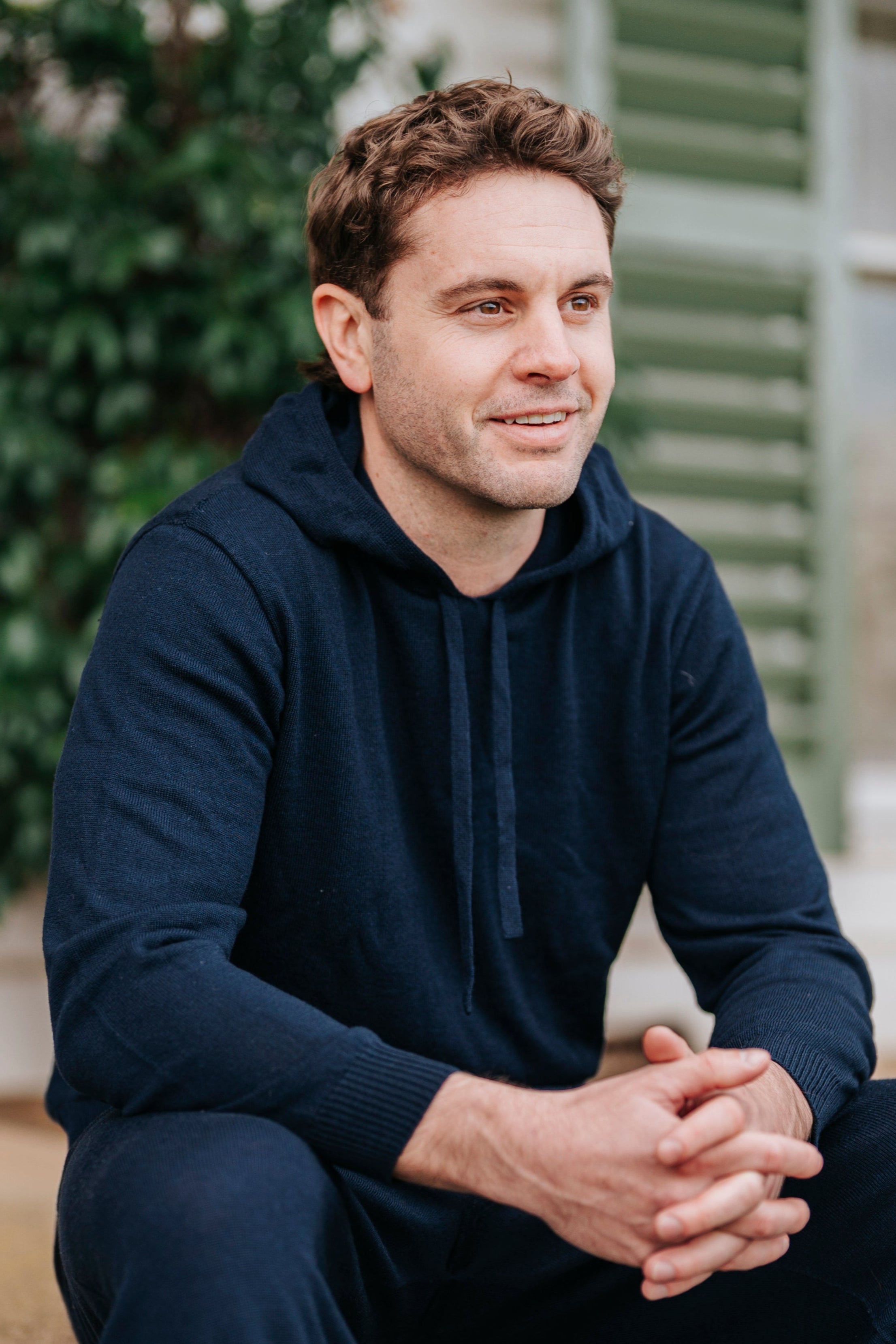 Man sitting on steps wearing a navy tracksuit with a house and greenery in the background
