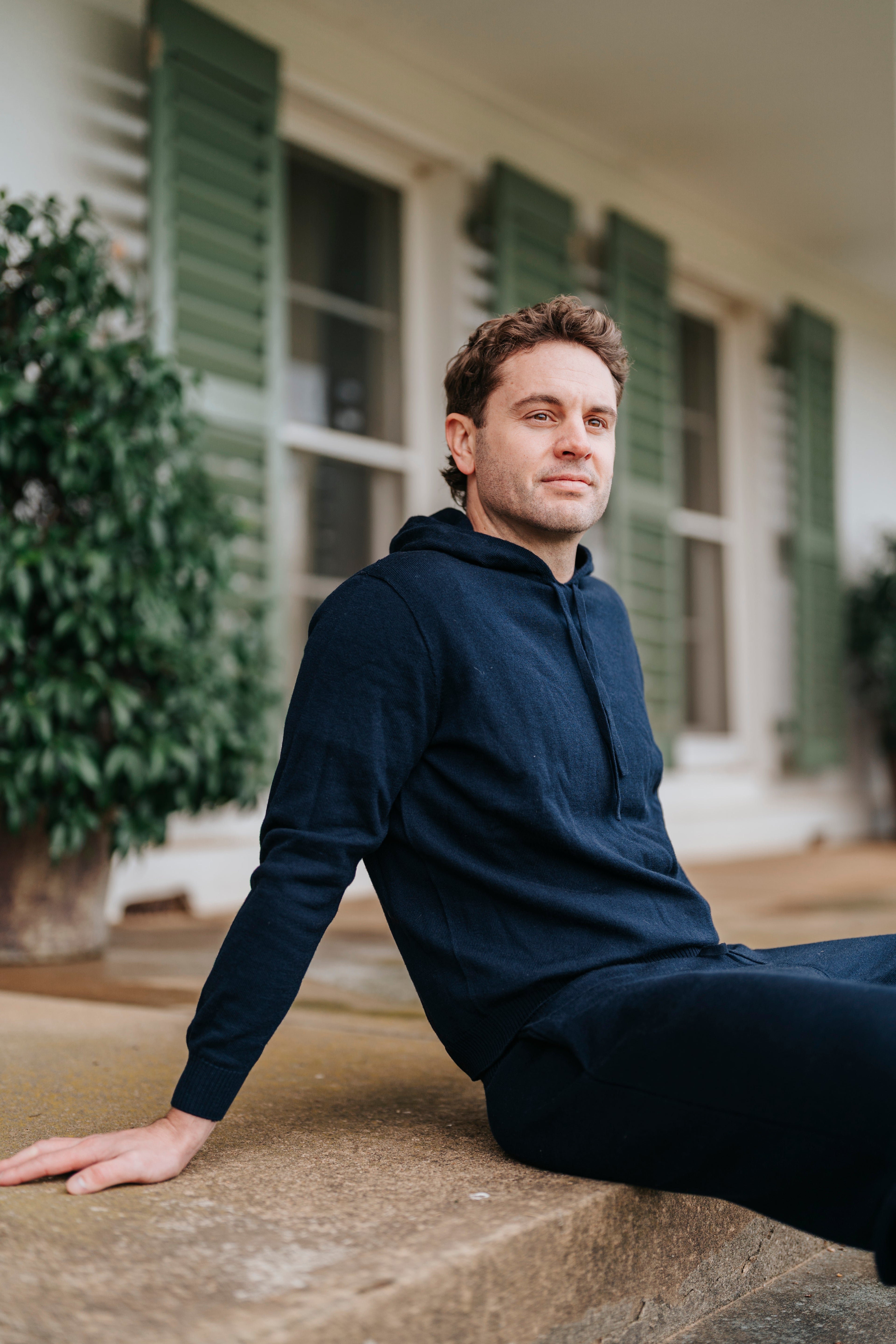 Man in a navy hoodie sitting on a stone step outdoors