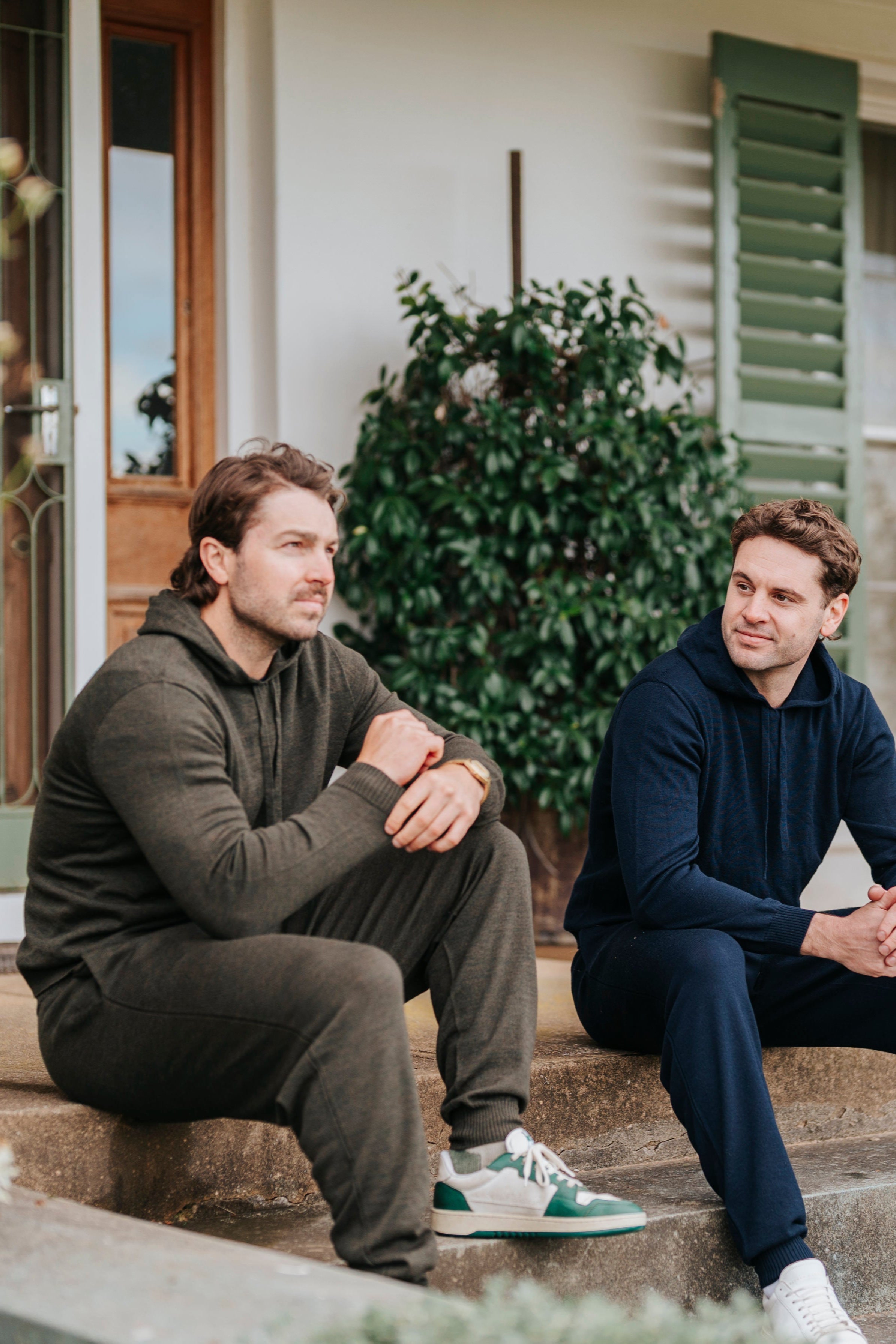 Two men sitting on a porch steps in front of a house.