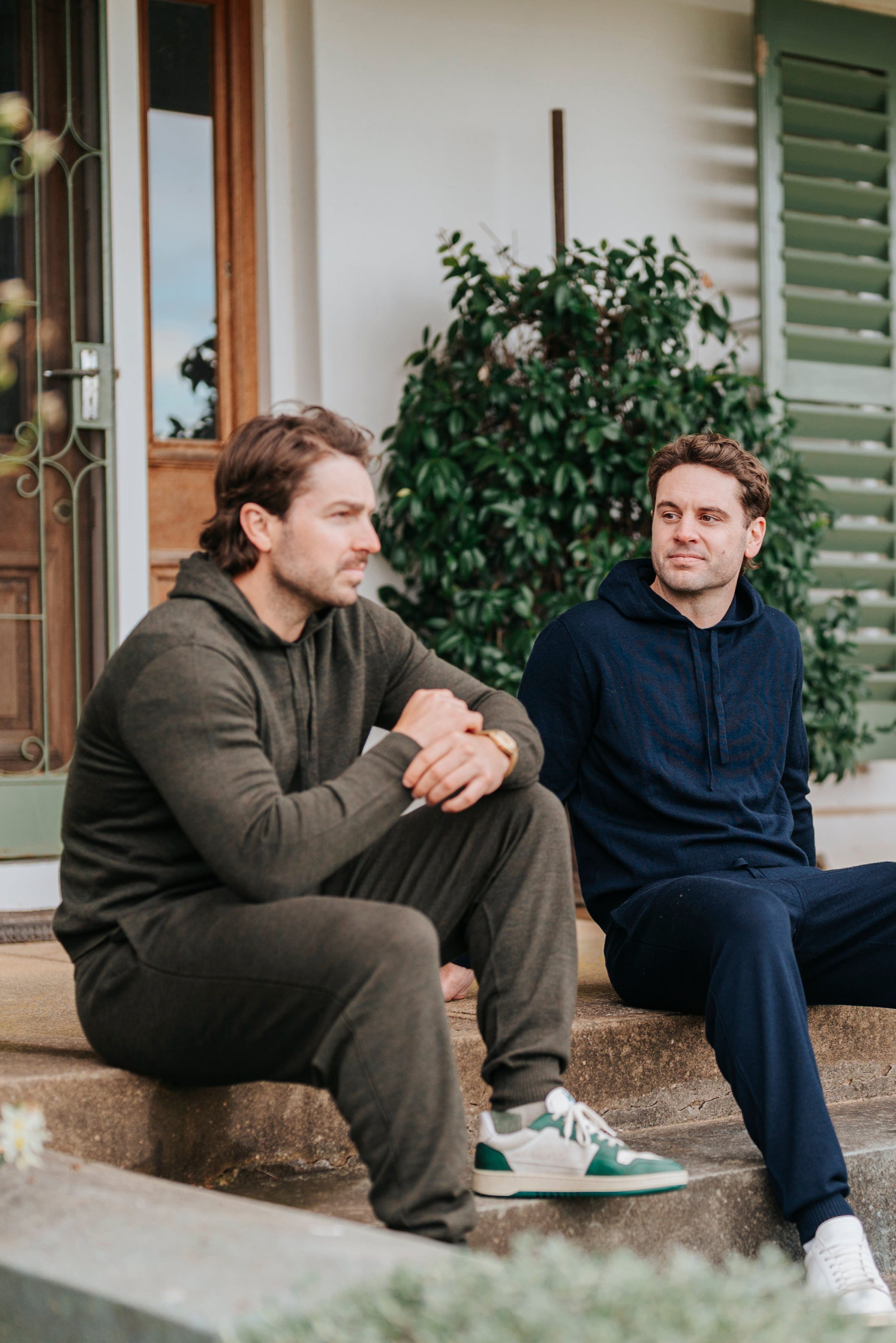 Two men sitting on a porch steps in front of a house in Merino wool