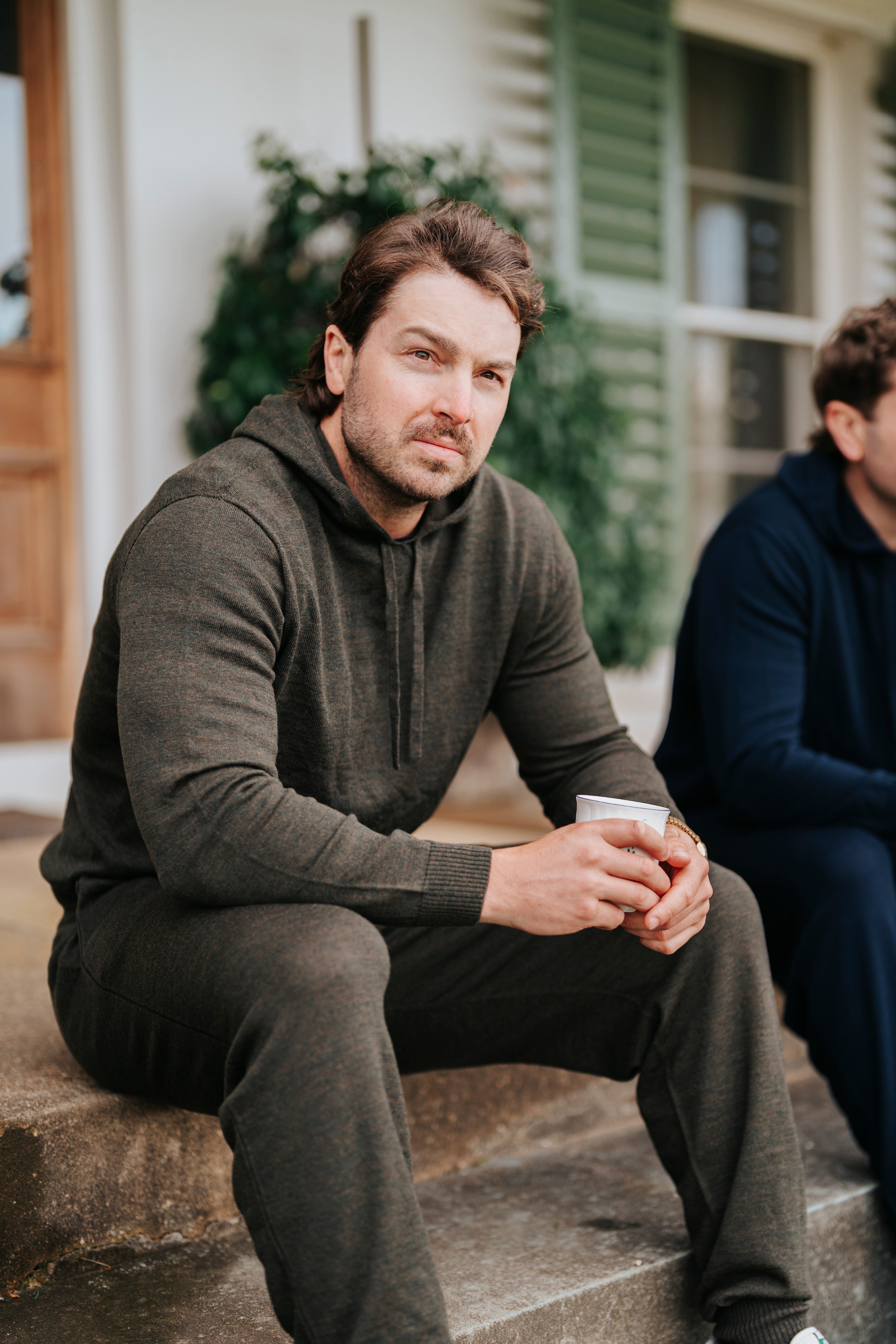 Man sitting on a stone step holding a cup, wearing merino wool hoodie and sweatpants