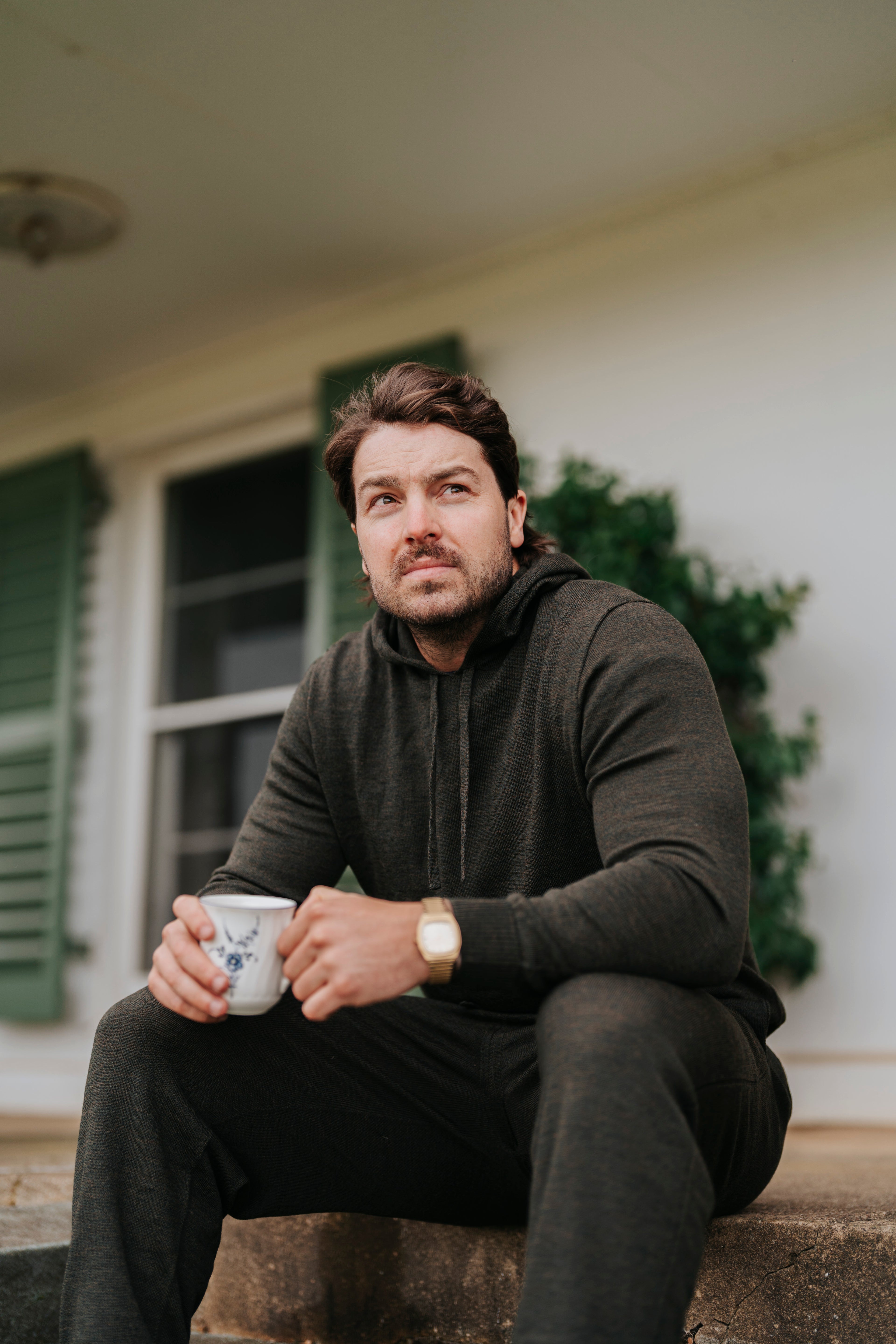 Man sitting on steps holding a mug in front of a house wearing Merino wool