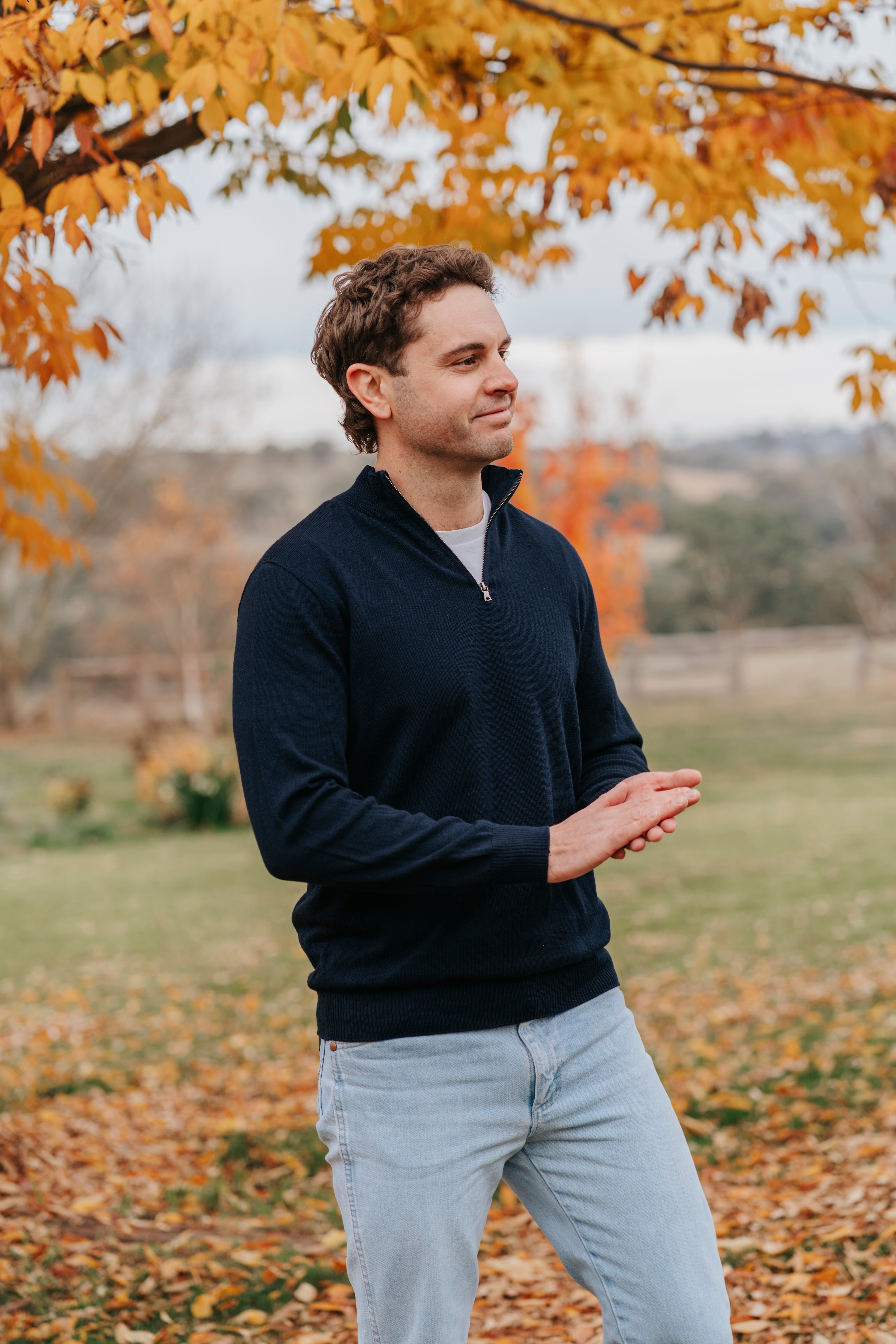 Man standing outdoors in a field with autumn leaves and trees in the background