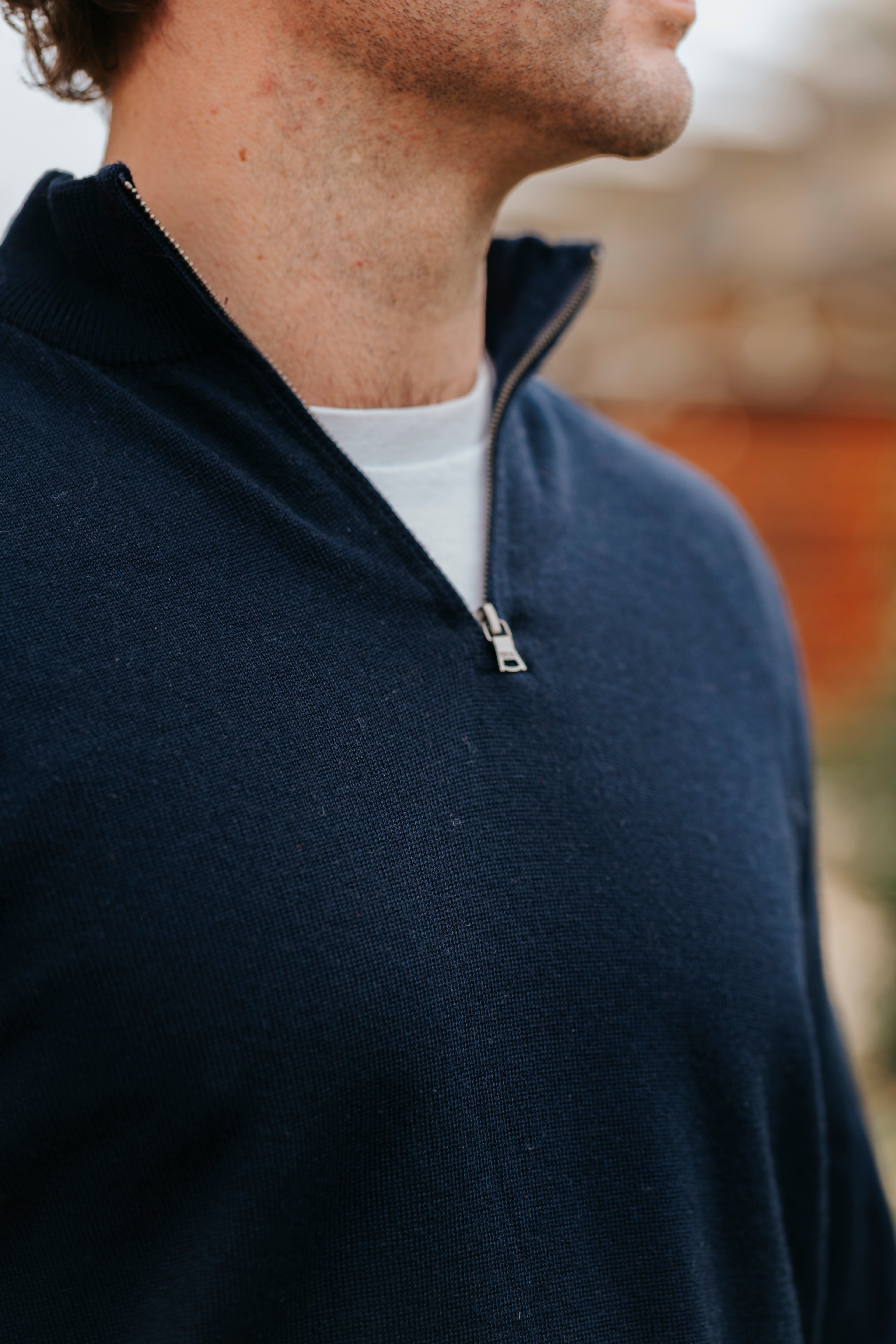 Person wearing a navy blue zip-up sweater over a white shirt with a blurred background