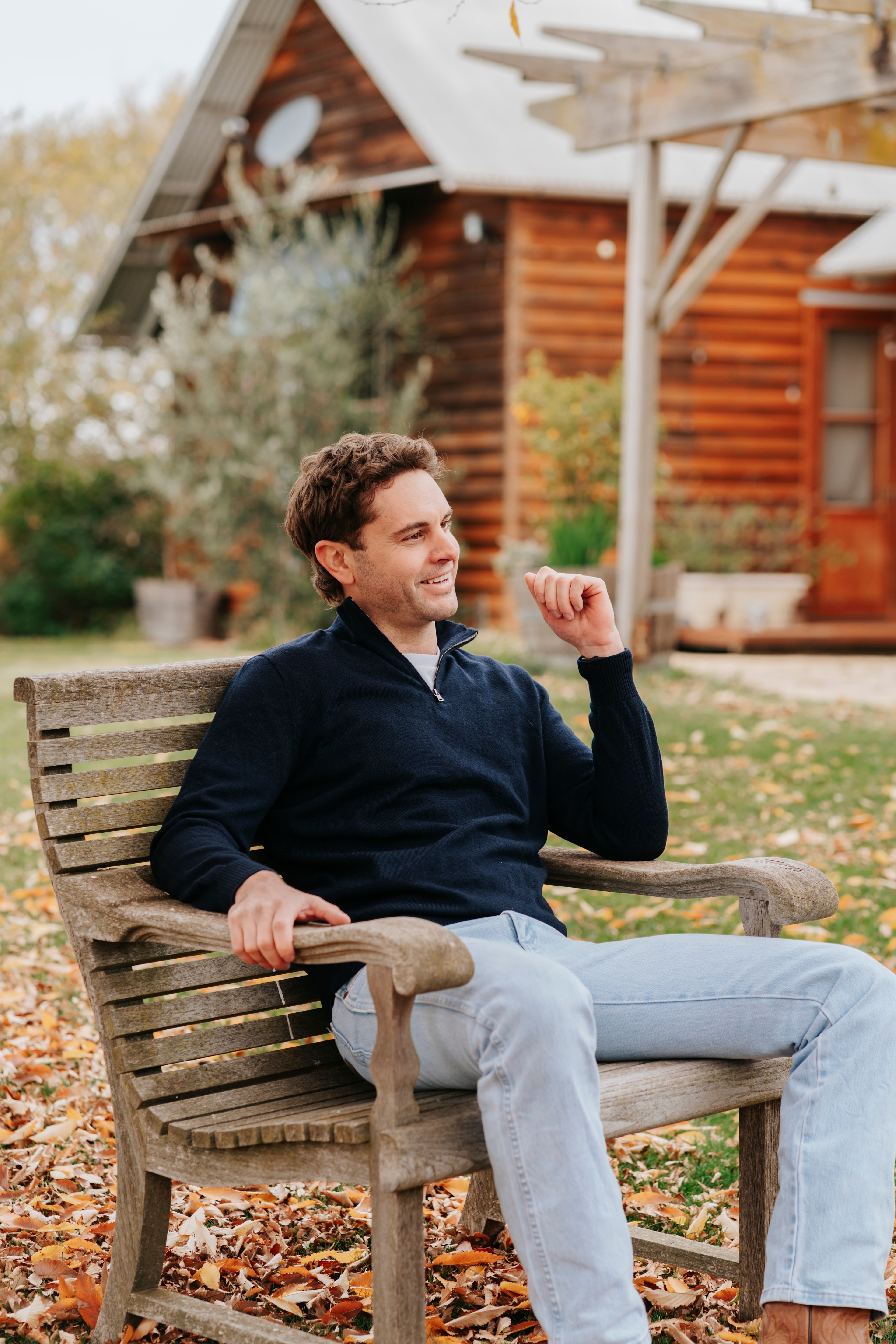 Man sitting on a wooden bench outdoors with a wooden cabin in the background