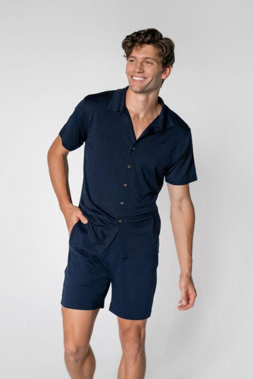 A man wearing a navy Merino button-up shirt and matching shorts, standing against a neutral background.