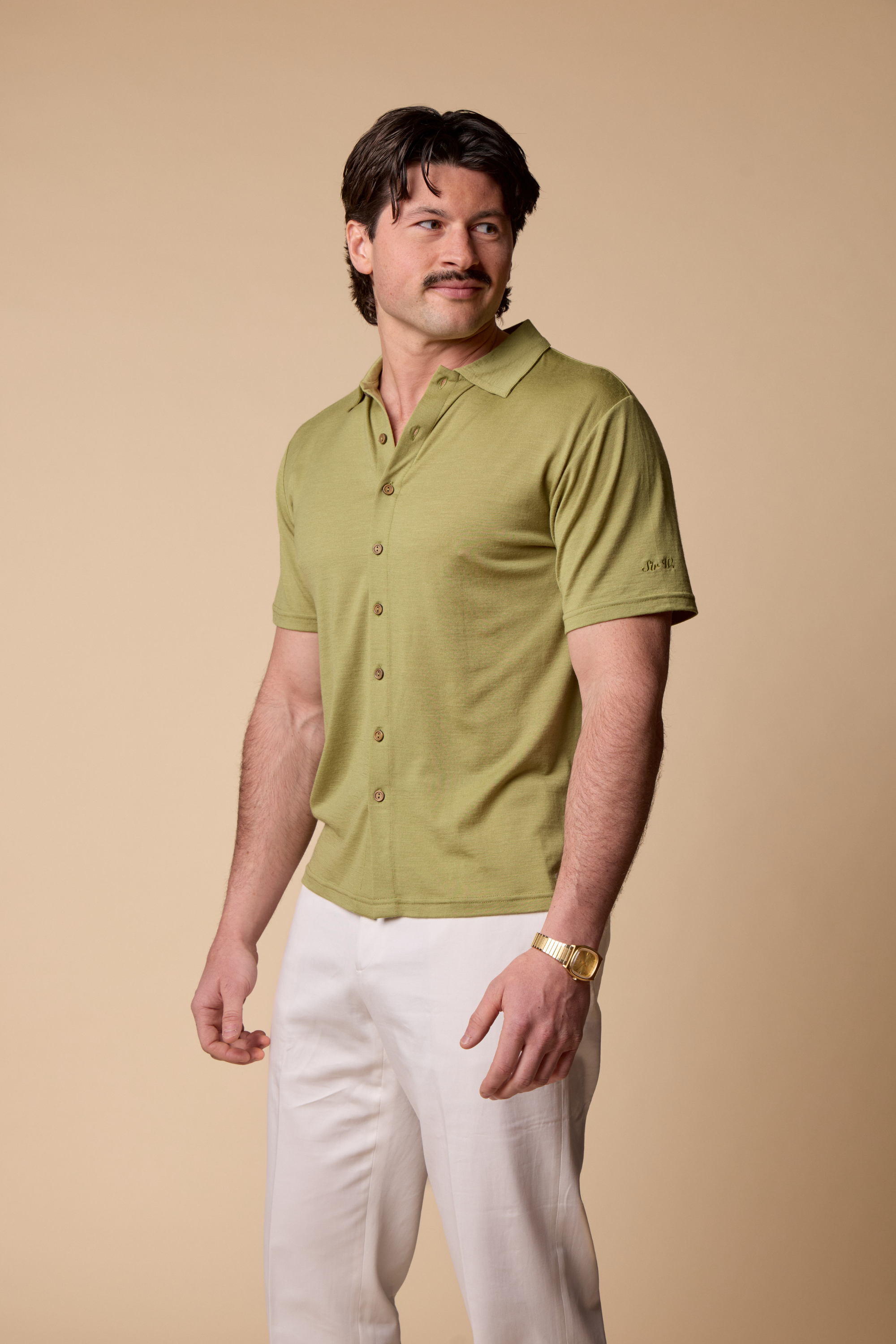 Man wearing a Sir W. Merino Bruce Olive Green shirt and white pants against a beige background