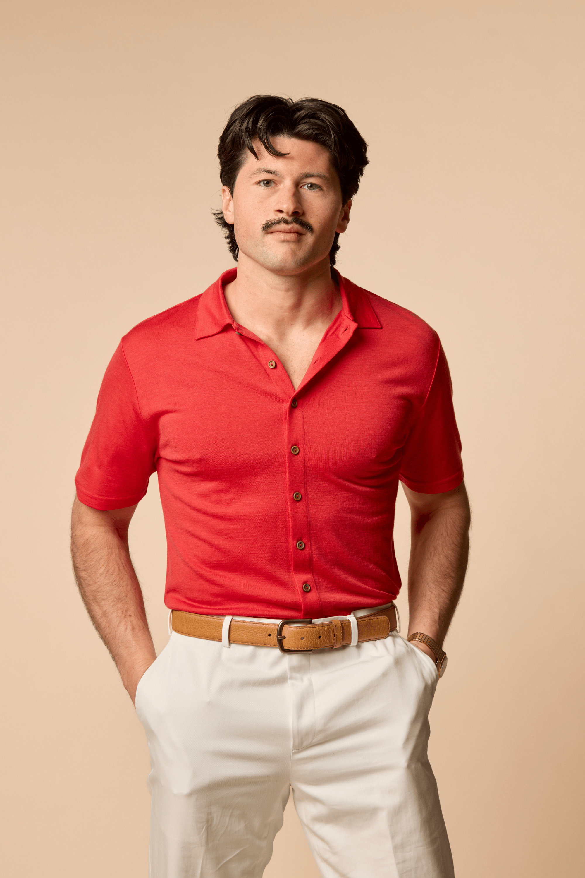 Man wearing a Sir W. Merino Bruce Poppy Red shirt and white pants against a beige background