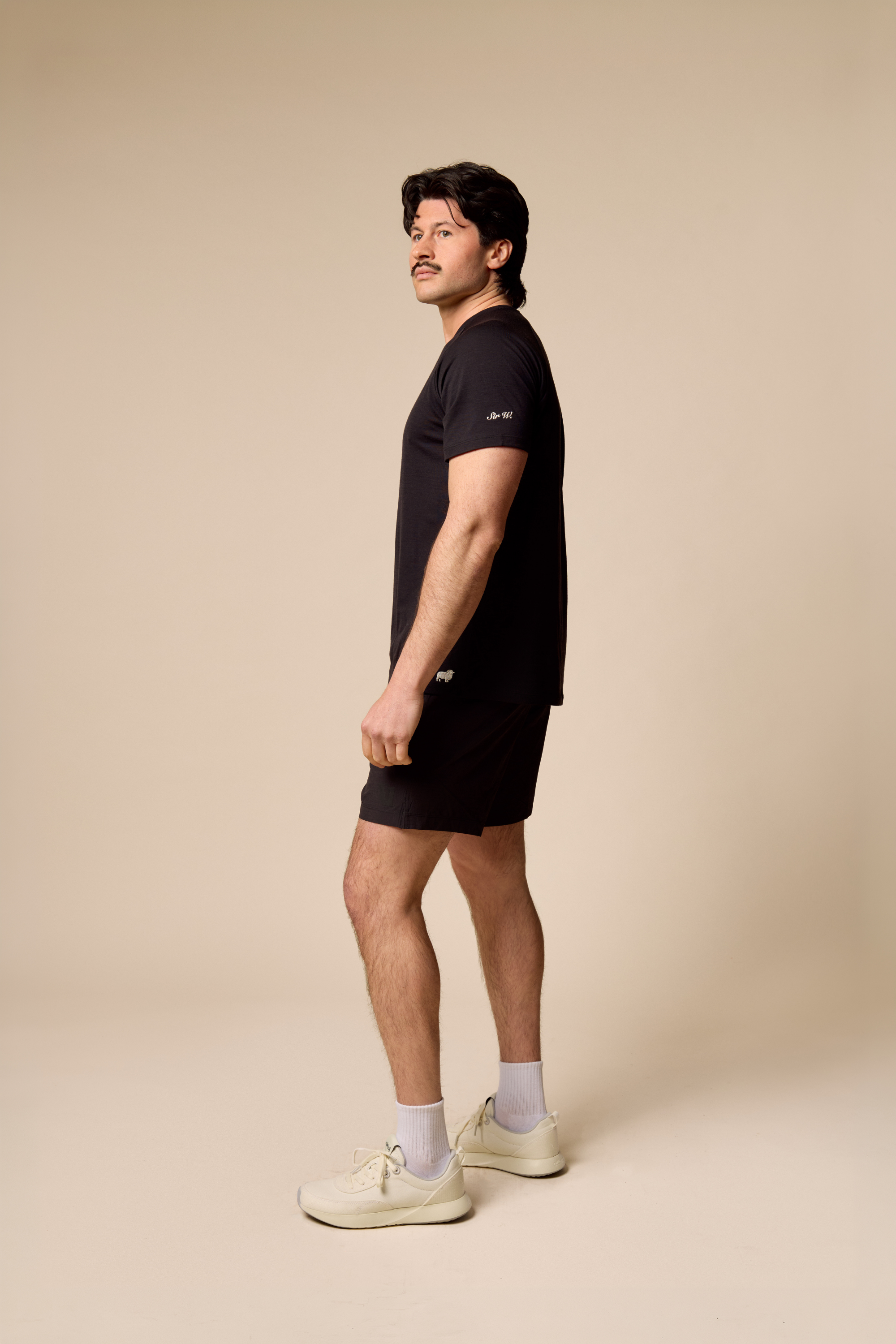 Man wearing a black Sir W. Merino t-shirt and shorts on a beige background