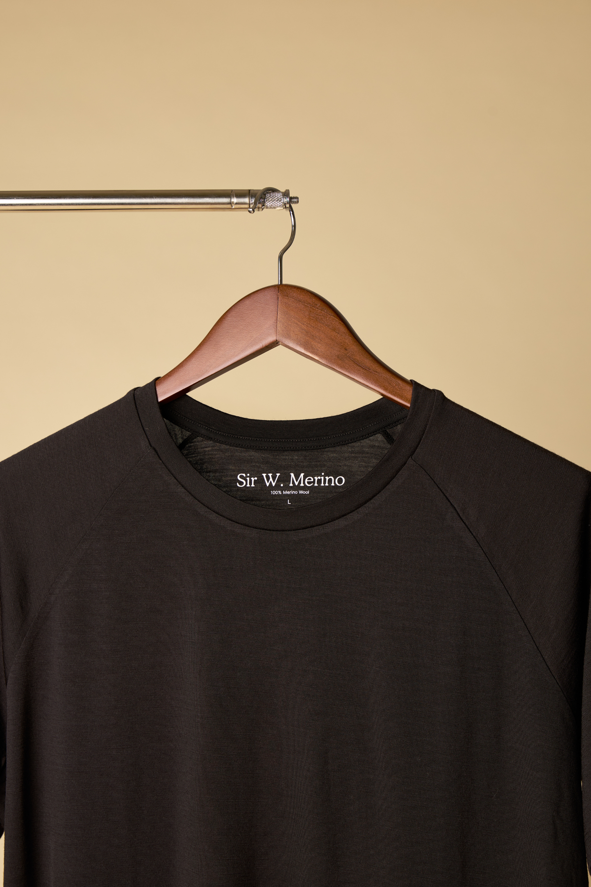 Sir W. Merino Black shirt on a wooden hanger against a beige background