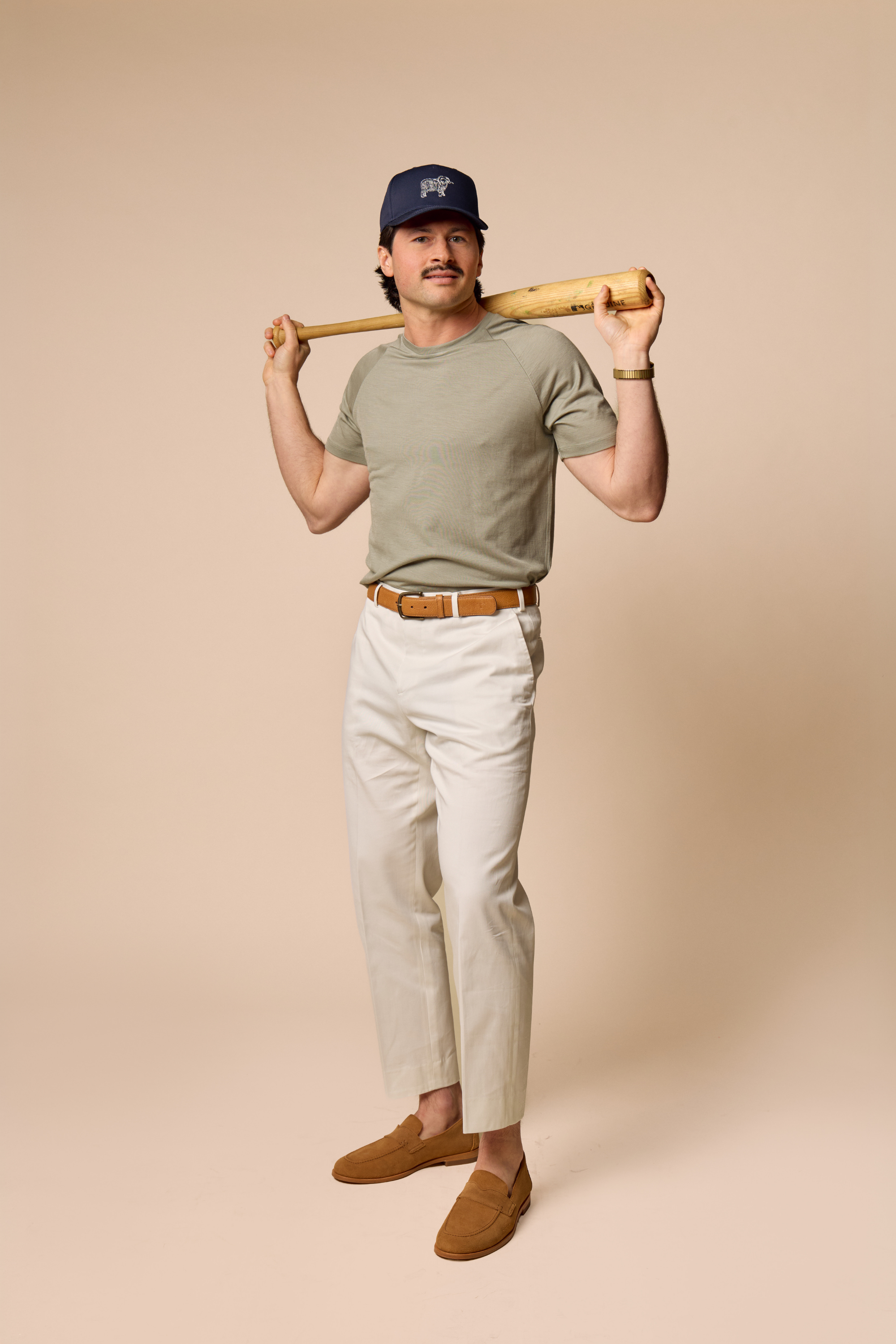 Man wearing Sir W. Merino cassius shadow grey tee and white pants with navy Sir W. cap while holding baseball bat