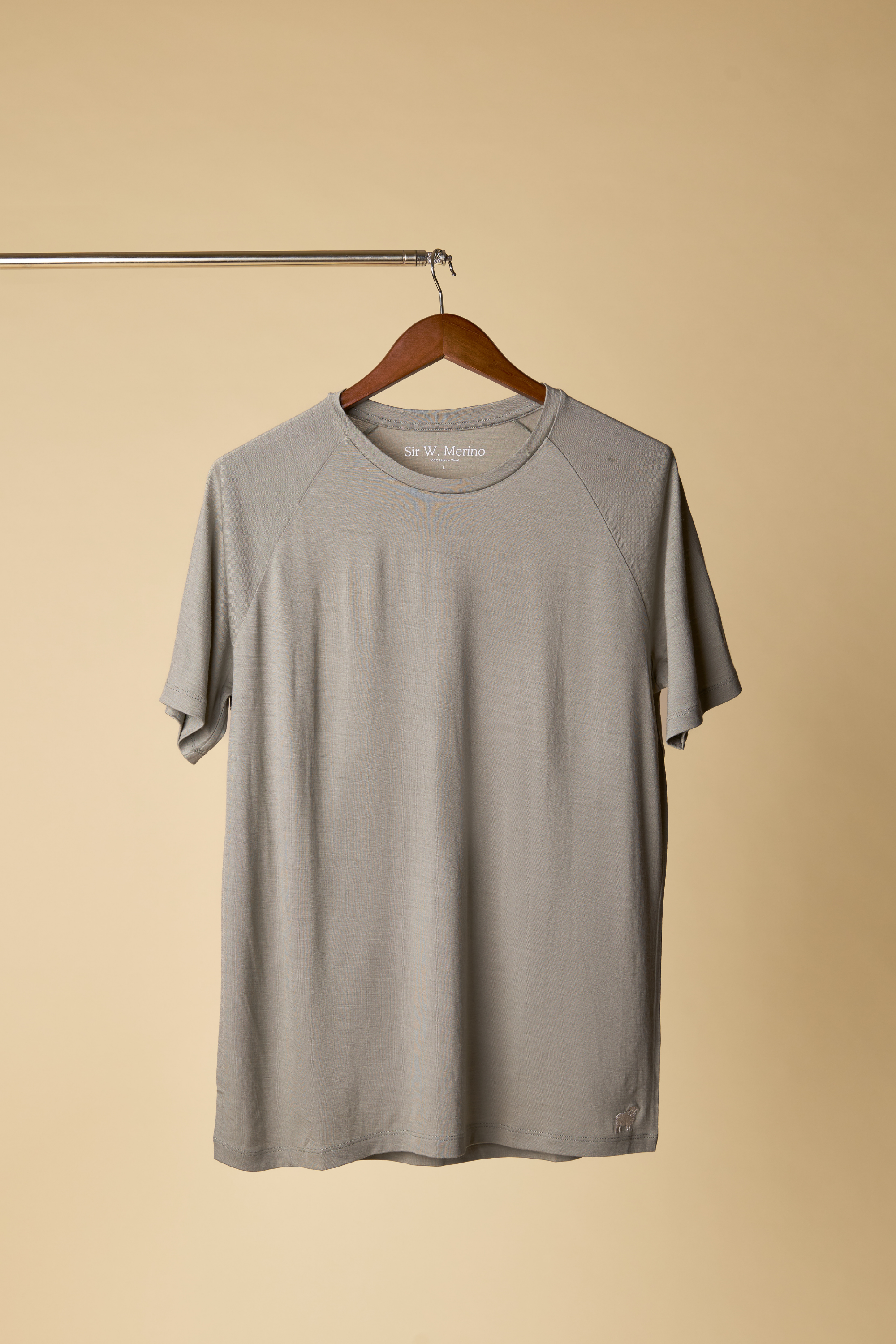 Sir W. Merino cassius shadow grey t-shirt hanging on a wooden hanger against a beige background