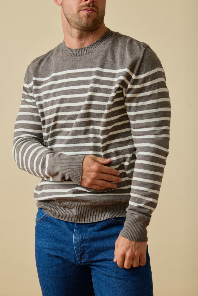Man wearing a gray and white striped Sir W. Merino sweater with blue jeans against a beige background