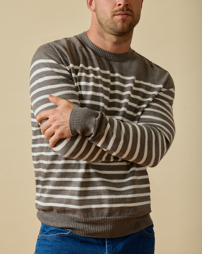Man wearing a gray and white striped Merino wool sweater with blue jeans against a beige background