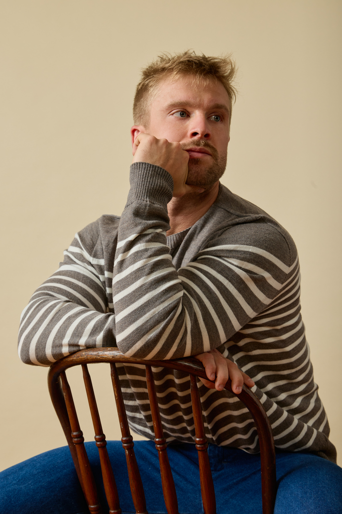 Man sitting on a chair wearing a striped Sir W. Merino sweater against a beige background