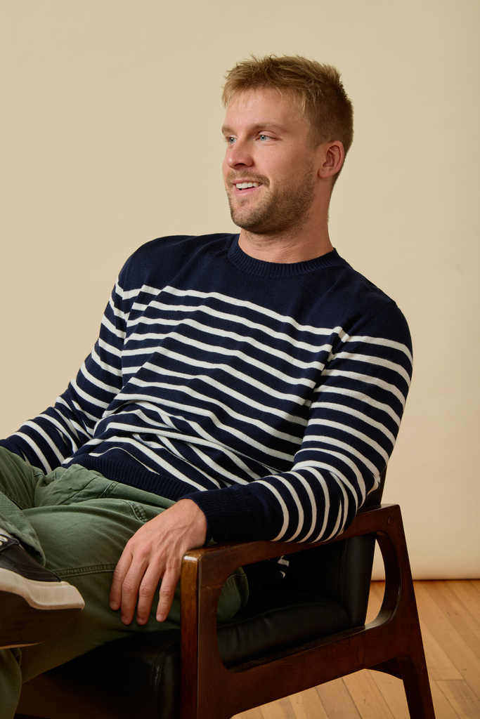 Man wearing a striped Sir W. Merino sweater sitting on a chair against a plain background
