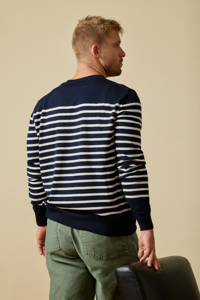 Man wearing a navy and white striped Sir W. Merino sweater with green pants against a beige background