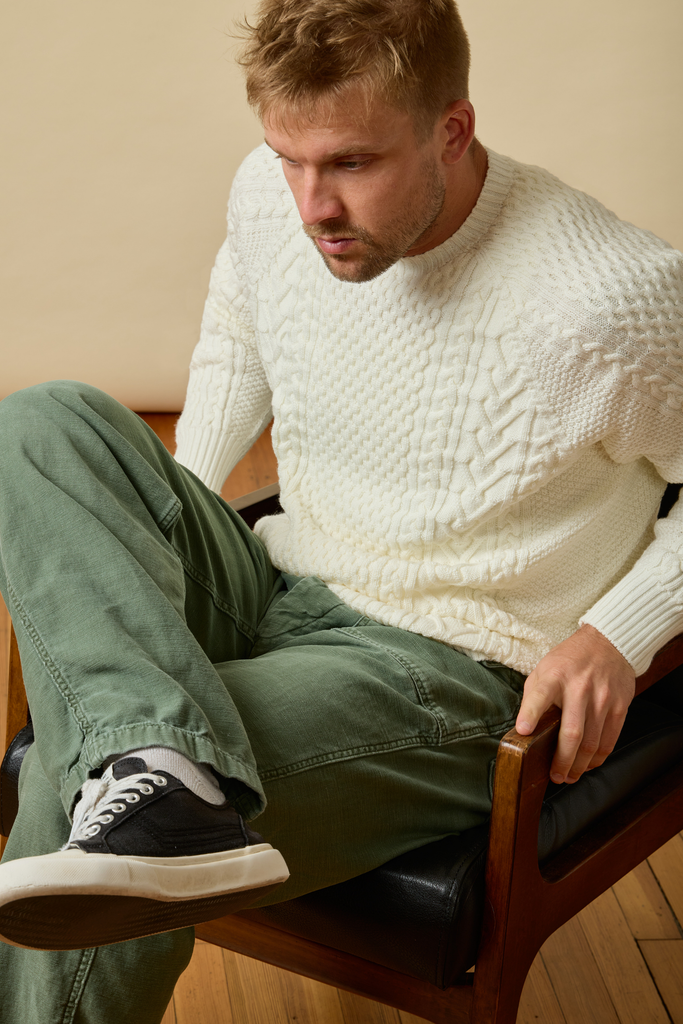 Man sitting on a chair wearing a white Sir W. Merino sweater and green pants.