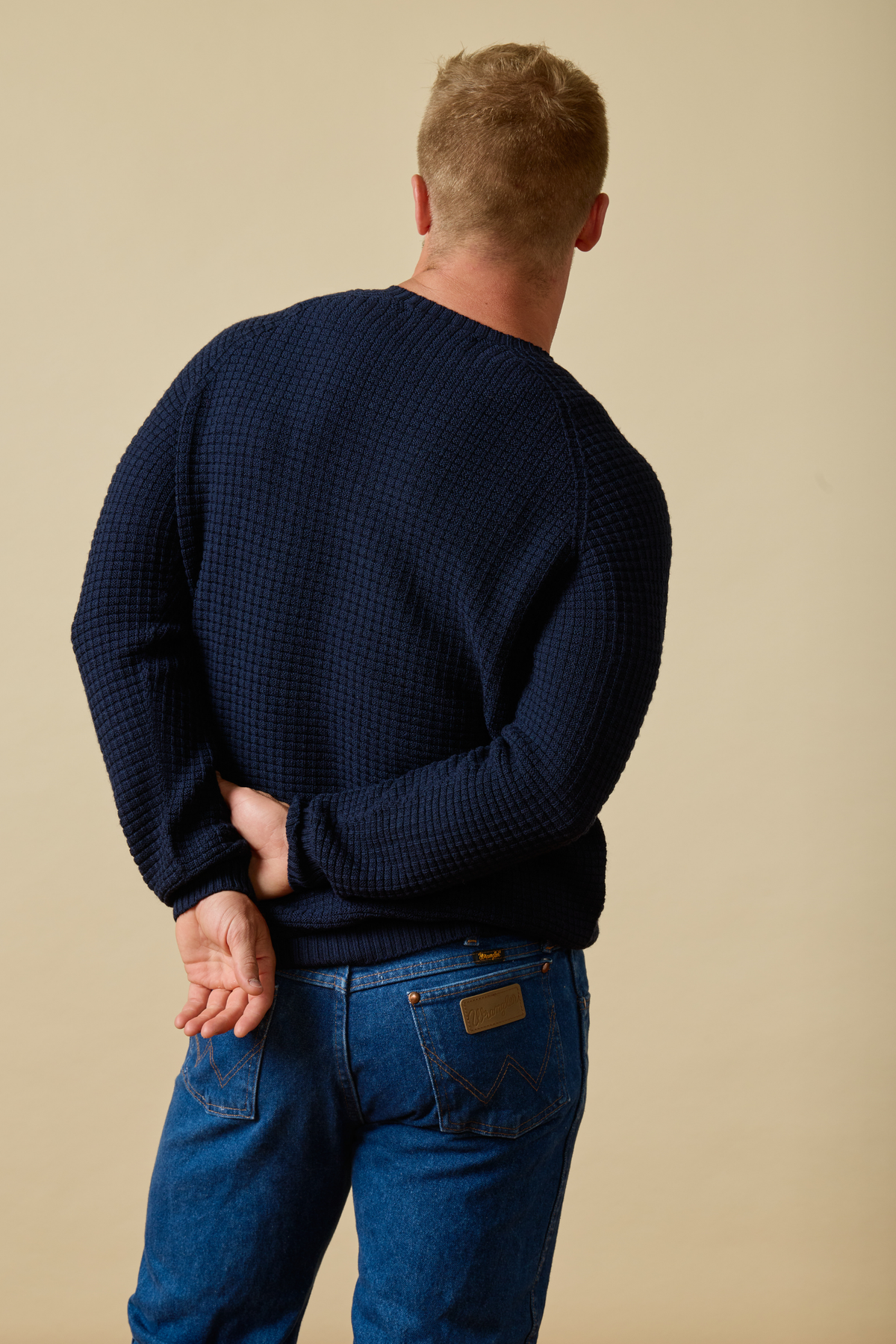 Man wearing a navy Sir W. Merino sweater and blue jeans against a beige background #color_navy