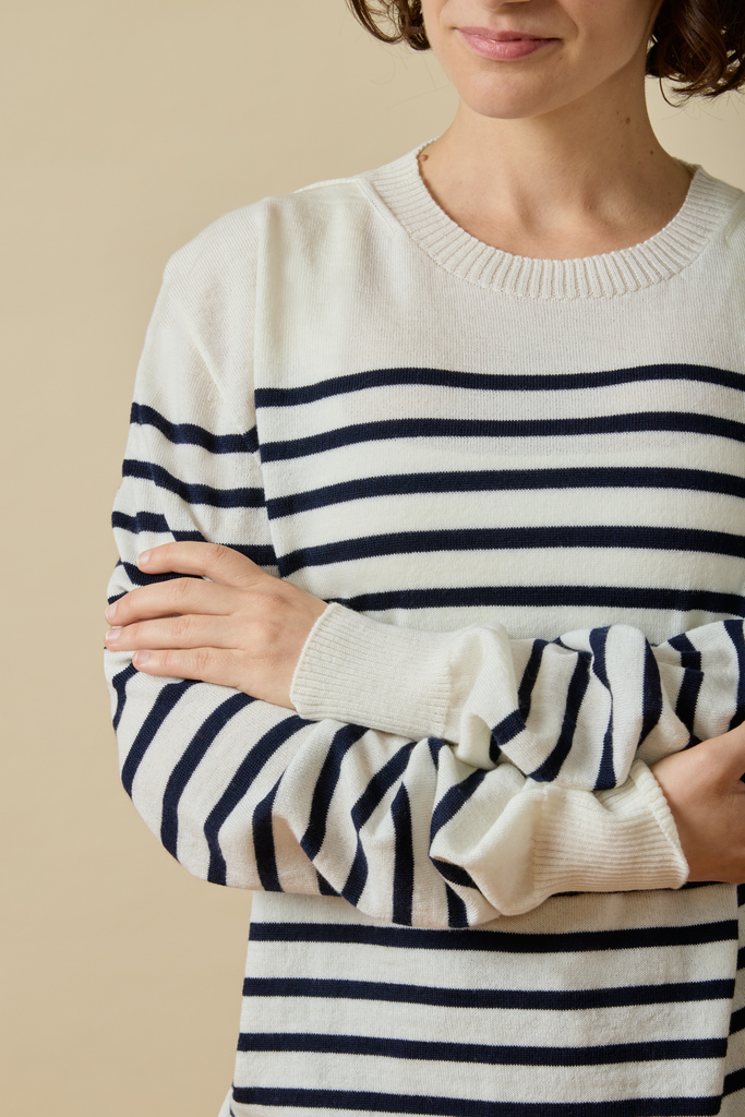 Person wearing a white Sir W. Merino sweater with navy blue stripes against a beige background