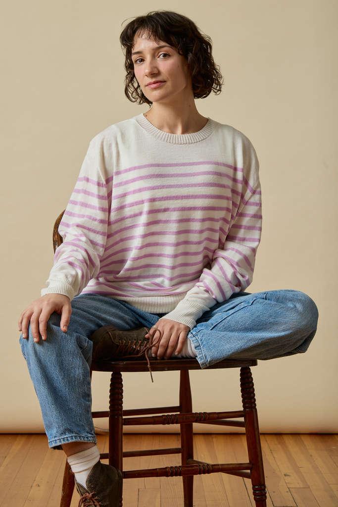 Woman wearing a striped Sir W. Merino sweater and jeans sitting on a wooden stool against a beige wall.