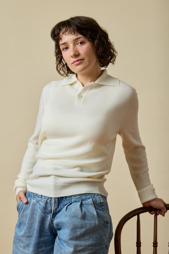 Woman wearing a white Sir W. Merino sweater and blue jeans against a beige background