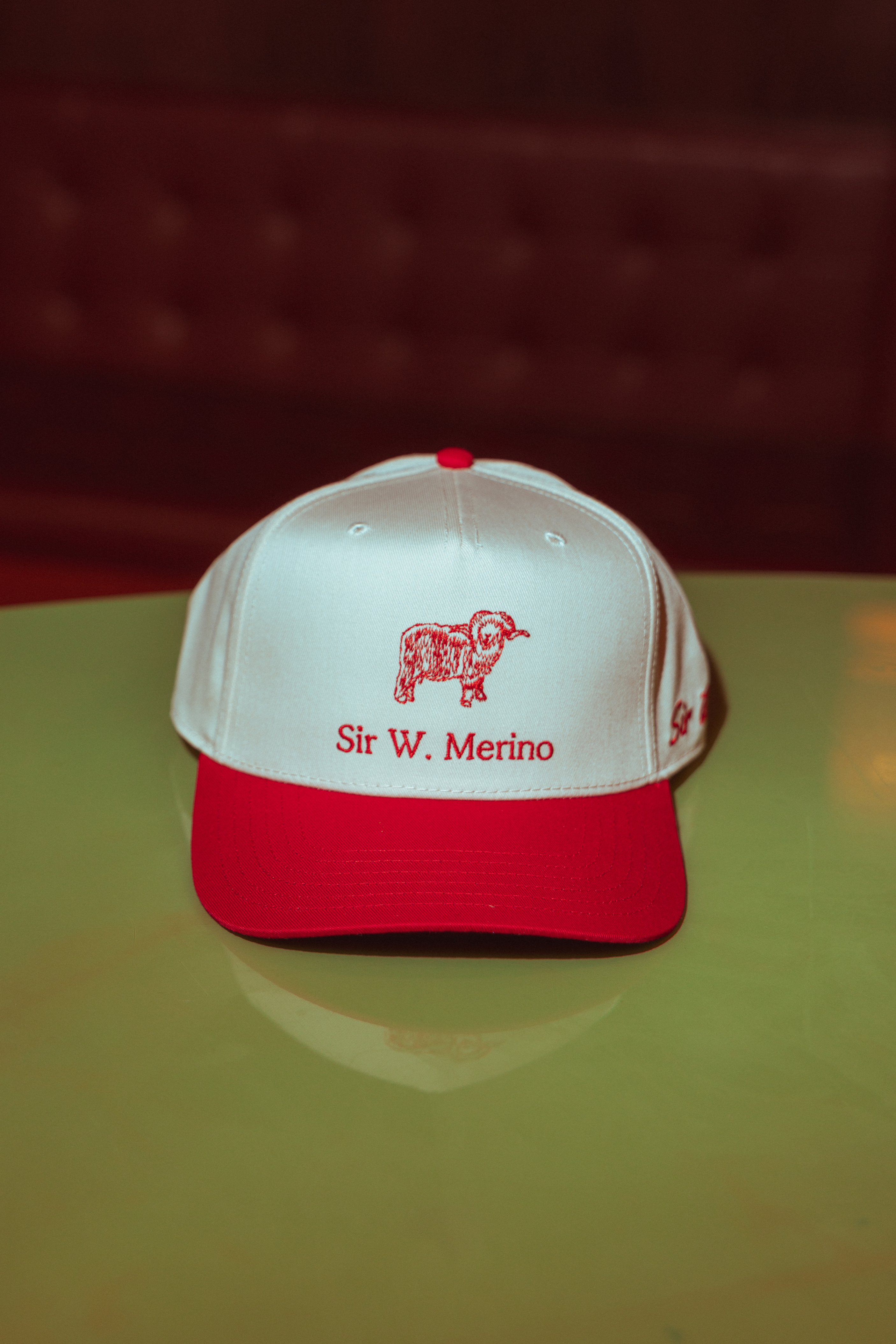 White and red cap with 'Sir W. Merino' logo on a reflective surface.