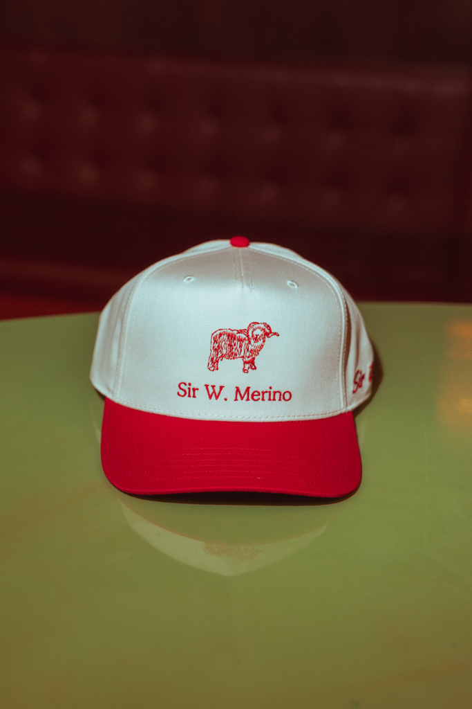 White and red cap with 'Sir W. Merino' logo on a reflective surface.