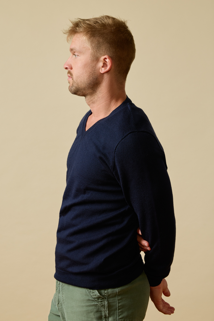 Man wearing a navy Merino wool sweater and green pants against a beige background