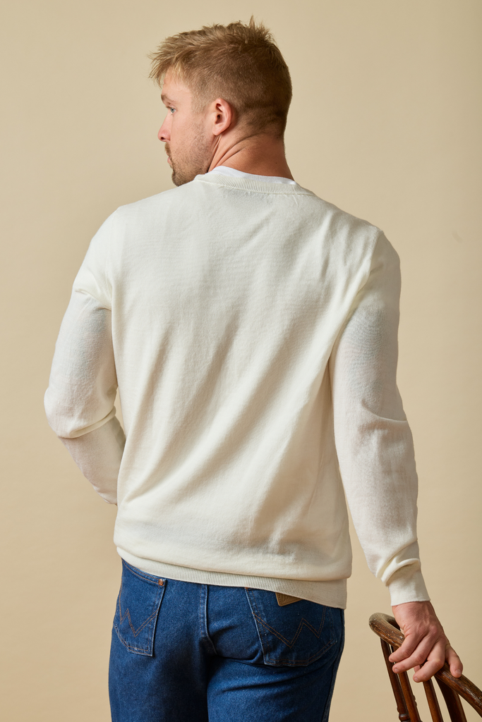 Man wearing a white Merino wool sweater and blue jeans against a beige background