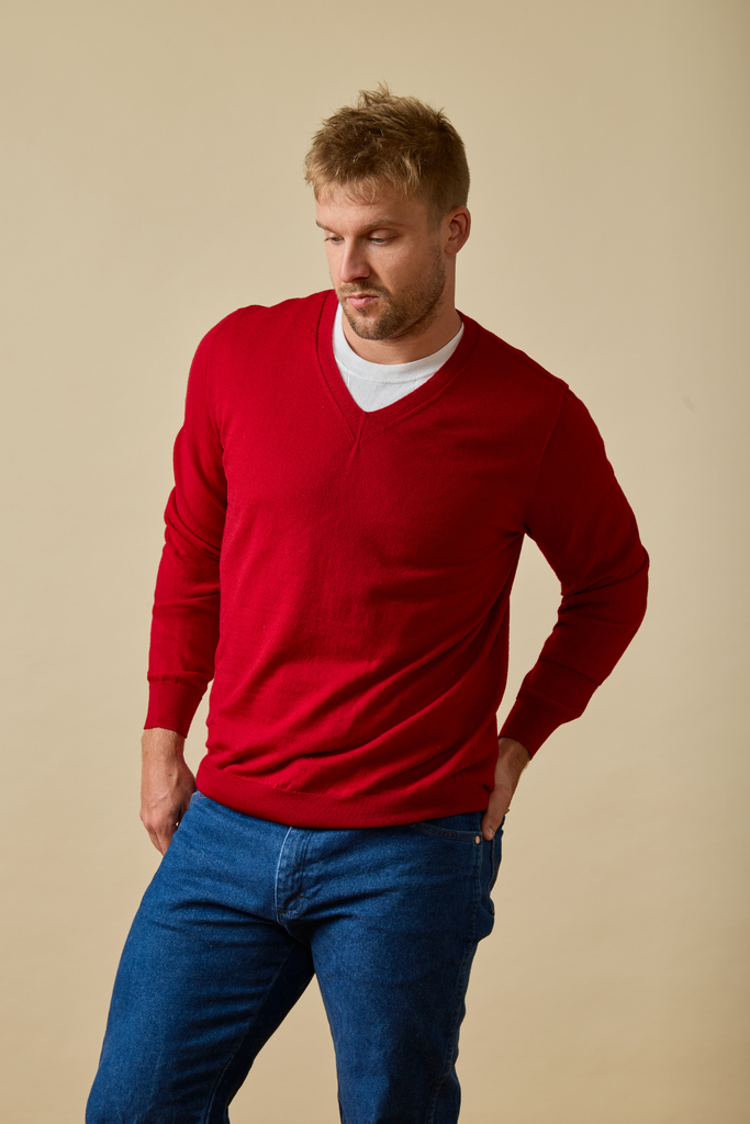 Man wearing a red Merino wool sweater and blue jeans against a beige background