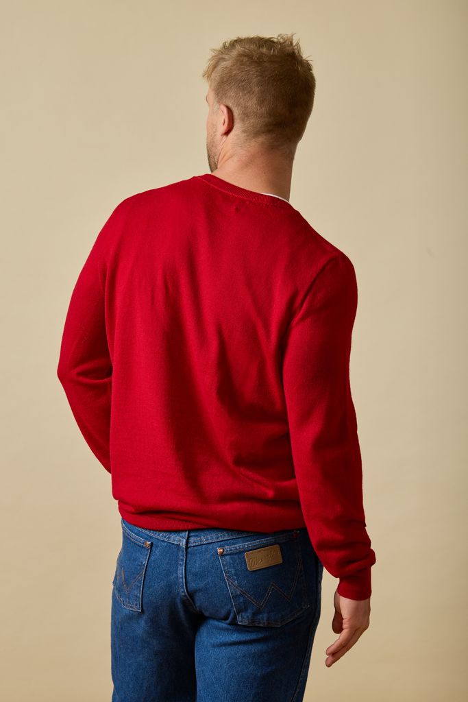 Man wearing a red Merino wool sweatshirt and blue jeans against a beige background