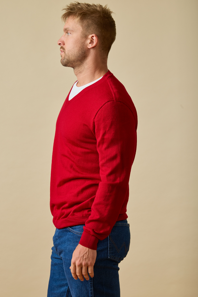 Man wearing a red Merino wool sweater and blue jeans against a beige background