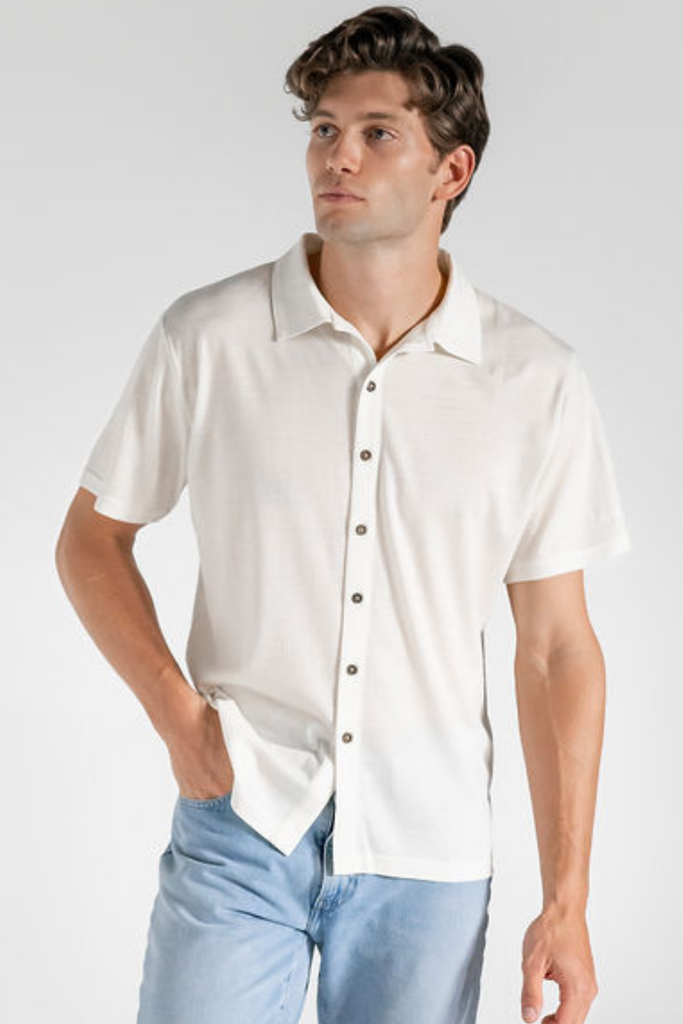 A man wearing a white merino wool shirt and light blue jeans, standing against a neutral background.