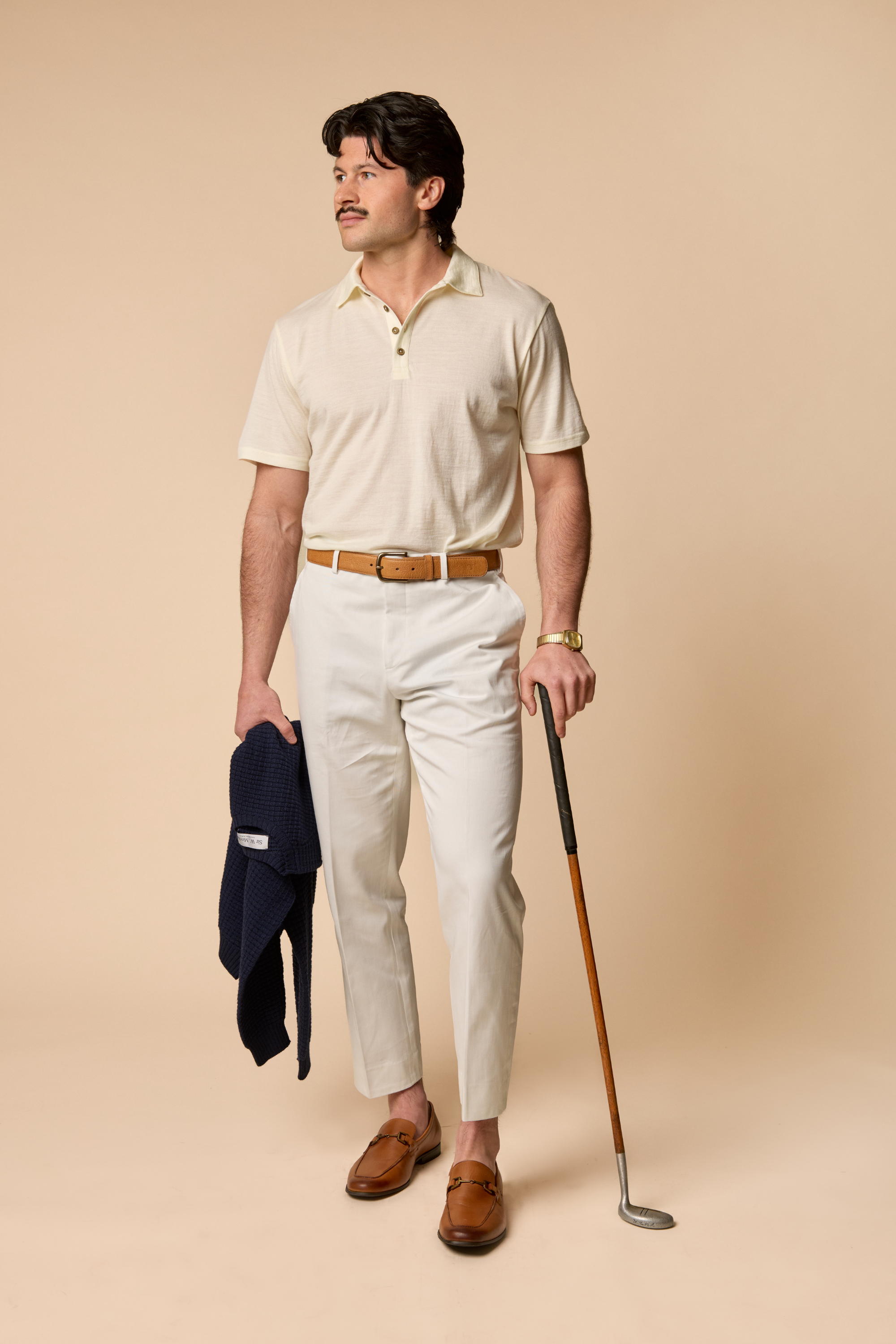 Man in Sir W golf attire holding a navy sweater and golf club 