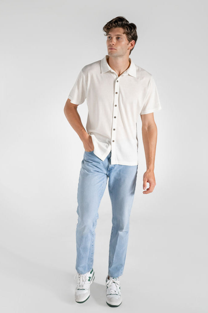 A man wearing a white merino wool shirt and light blue jeans, standing against a neutral background.