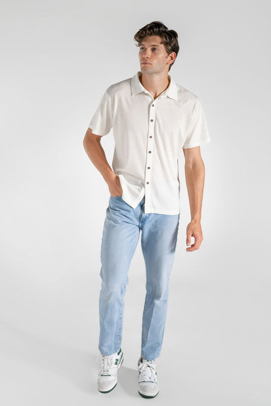 A man wearing a white merino wool shirt and light blue jeans, standing against a neutral background.