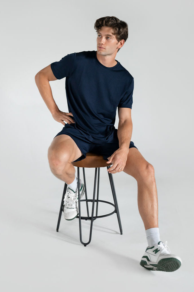 A person wearing navy blue merino wool lounge shorts and tee sitting down relaxed