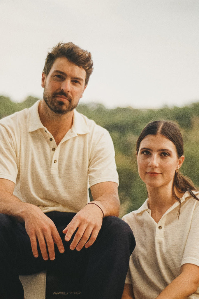 A man wearing a white merino wool polo shirt with a relaxed collar and next to a women in the same shirt