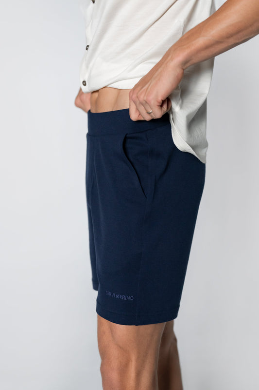 A person wearing navy blue merino wool lounge shorts and a white shirt.