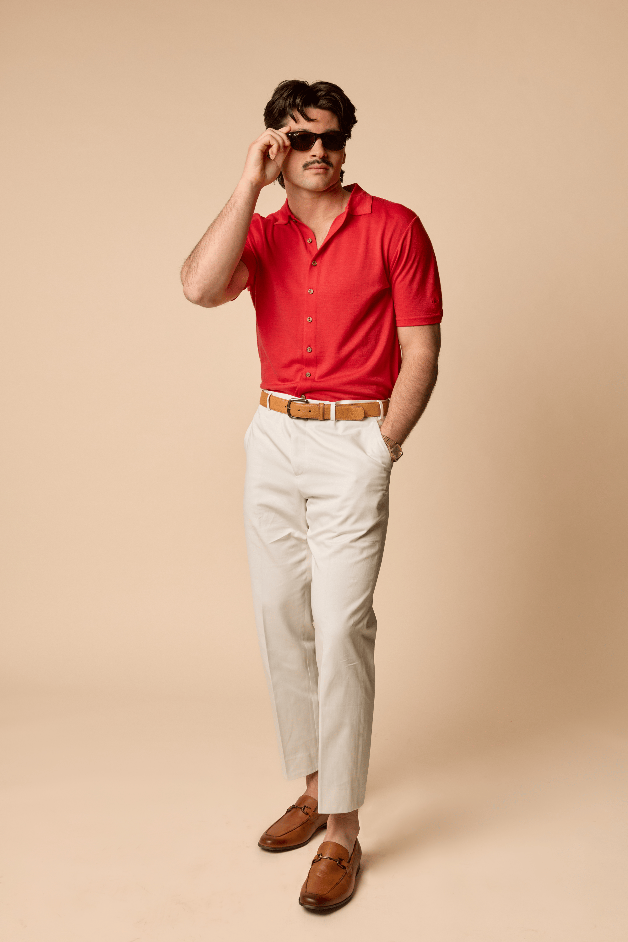 Man wearing a Sir W. Merino Bruce Poppy Red shirt, white pants, and brown shoes
